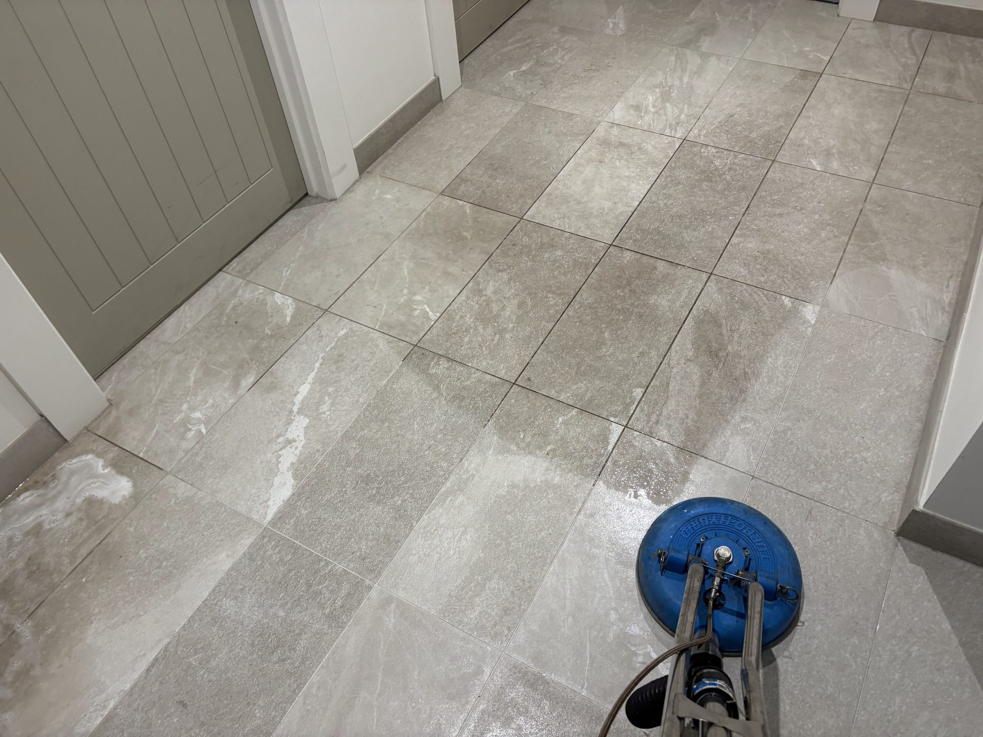 Tile floor half cleaned with a rotary steam tool, showing the clean and dirty sections