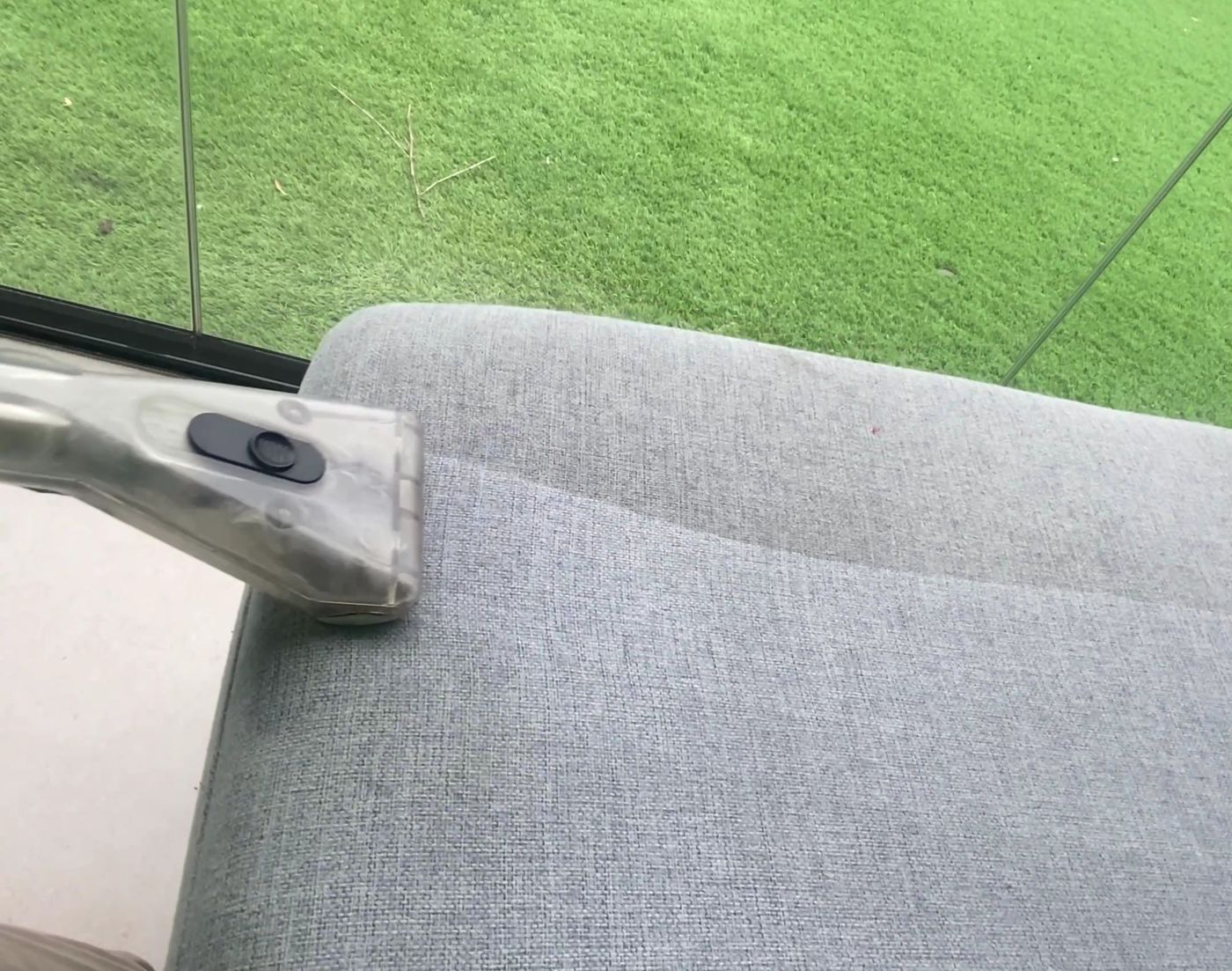 Grey fabric lounge being steam cleaned with an upholstery tool